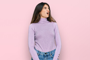 Young beautiful teen girl wearing turtleneck sweater angry and mad screaming frustrated and furious, shouting with anger. rage and aggressive concept.