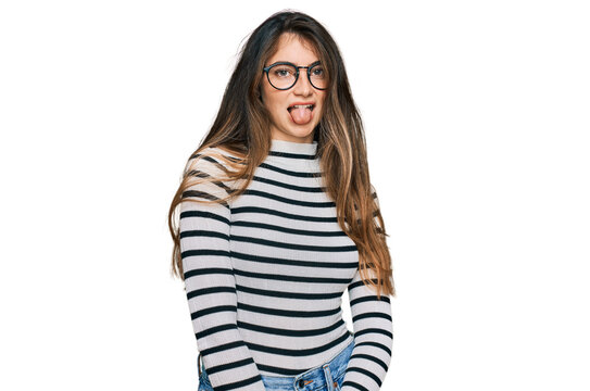 Young beautiful teen girl wearing casual clothes and glasses sticking tongue out happy with funny expression. emotion concept.