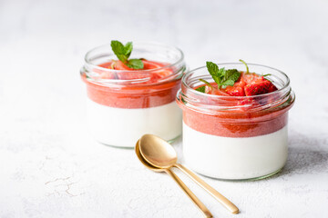 Panna cotta in glass jars with strawberry sauce and mint.