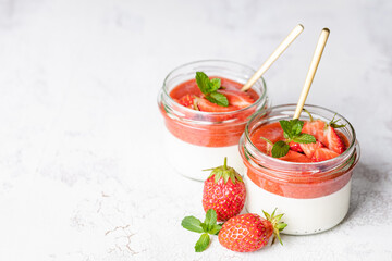 Panna cotta in glass jars with strawberry sauce and mint on white table.