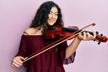 Young brunette musician woman with curly hair playing violin smiling and laughing hard out loud because funny crazy joke.