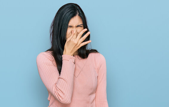 Young Hispanic Woman Wearing Casual Clothes Smelling Something Stinky And Disgusting, Intolerable Smell, Holding Breath With Fingers On Nose. Bad Smell