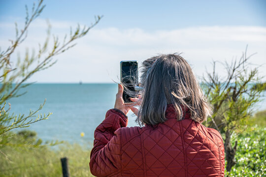 Vendée, FRANCE; May 27, 2021: An elderly person with white hair takes a picture of the ocean with his smartphone in Saint-Gilles-Croix-de-Vie. 