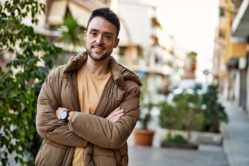 Obraz premium Young hispanic man smiling happy with arms crossed gesture at the city.