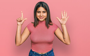 Young hispanic girl wearing casual t shirt showing and pointing up with fingers number seven while smiling confident and happy.