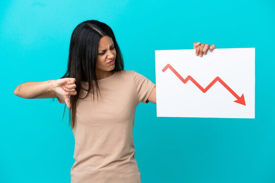 Young woman over isolated background holding a sign with a decreasing statistics arrow symbol and doing bad signal