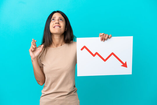 Young woman over isolated background holding a sign with a decreasing statistics arrow symbol with fingers crossing