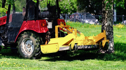 Yellow mower. A small tractor mows the lawn. Landscaping of the area between the houses. City garden.