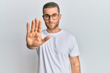 Young caucasian man wearing casual clothes and glasses doing stop sing with palm of the hand....
