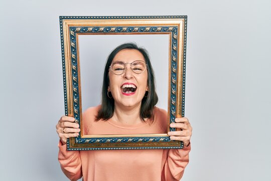 Middle age hispanic woman holding empty frame smiling and laughing hard out loud because funny crazy joke.