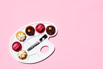 Creative still life of colorful macarons as a form of colors on art palette. Minimal abstract concept. Macarons pastry almond sweet on pink background