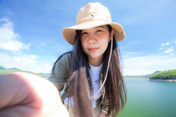 Young happy woman with backpack standing with raised hands and looking to the river. Woman traveling concept