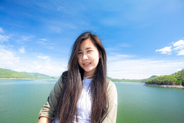 Young happy woman with backpack standing with raised hands and looking to the river. Woman traveling concept