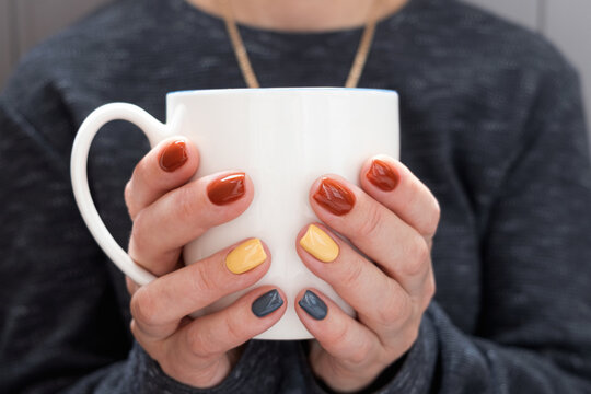 The girl warms up, holding a cup of coffee in her hands. Well-groomed hands beautiful manicure, design for any purpose. Blurred background.