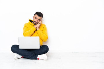 Caucasian man sitting on the floor with his laptop making sleep gesture in dorable expression