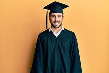 Young hispanic man wearing graduation cap and ceremony robe with a happy and cool smile on face. lucky person.