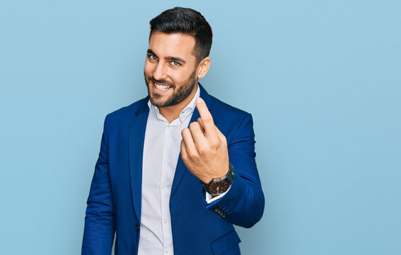 Young hispanic man wearing business jacket beckoning come here gesture with hand inviting welcoming happy and smiling