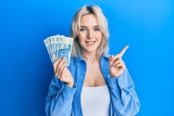Young blonde girl holding 50 polish zloty banknotes smiling happy pointing with hand and finger to the side