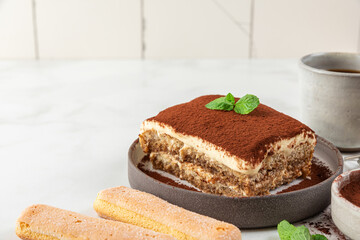 Homemade tiramisu cake with fresh mint on plate over white background. Delicious no bake italian dessert