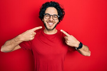 Fototapeta premium Handsome hispanic man wearing casual t shirt and glasses smiling cheerful showing and pointing with fingers teeth and mouth. dental health concept.