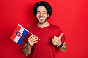 Handsome hispanic man holding croatia flag smiling happy and positive, thumb up doing excellent and approval sign