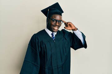 Handsome black man wearing graduation cap and ceremony robe smiling pointing to head with one finger, great idea or thought, good memory