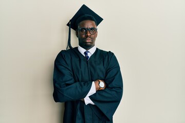 Handsome black man wearing graduation cap and ceremony robe skeptic and nervous, disapproving...