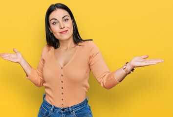Young hispanic woman wearing casual clothes clueless and confused expression with arms and hands...