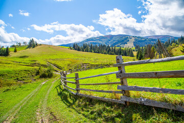 Fototapeta na wymiar country road near wooden fence against mountains and forests background. Countryside