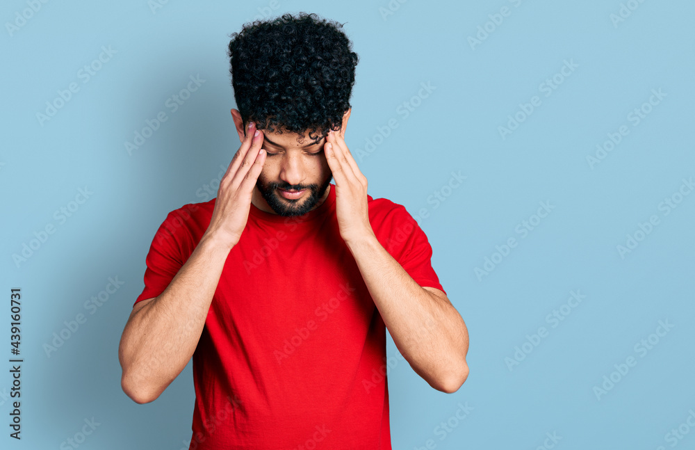 Sticker young arab man with beard wearing casual red t shirt with hand on head for pain in head because stre