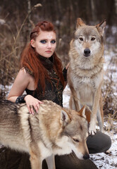 Female viking warrior with painted face and with two wolves in winter forest