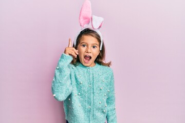 Little beautiful girl wearing cute easter bunny ears pointing finger up with successful idea. exited and happy. number one.
