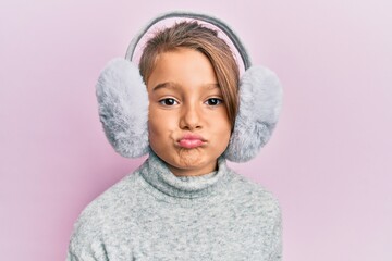 Little beautiful girl wearing fluffy earmuff looking at the camera blowing a kiss being lovely and sexy. love expression. - obrazy, fototapety, plakaty