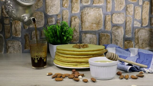 Moroccan or Algerian pancakes named Baghrir in arabic with honey syrup decorated with walnuts and almond and woman pouring tea