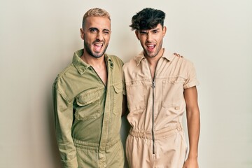 Homosexual gay couple standing together wearing casual jumpsuit winking looking at the camera with sexy expression, cheerful and happy face.