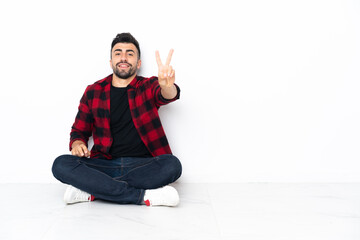 Young handsome man sitting on the floor smiling and showing victory sign