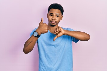 Young african american man wearing casual blue t shirt doing thumbs up and down, disagreement and...