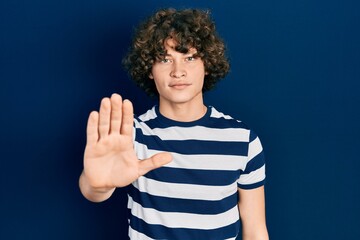 Handsome young man wearing casual striped t shirt doing stop sing with palm of the hand. warning...