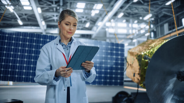Female Engineer Uses Tablet Computer while Working on Satellite Construction. Aerospace Agency Manufacturing Facility: Scientists Build, Assemble Spacecraft for Space Exploration, Observation Mission