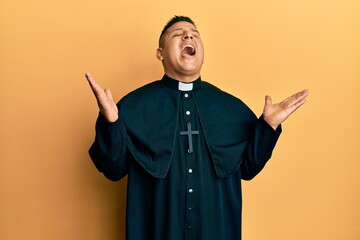 Young latin priest man standing over yellow background celebrating mad and crazy for success with...