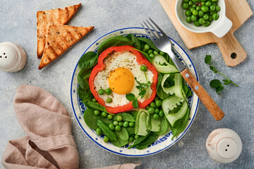 Red bell peppers stuffed with eggs, spinach leaves, green peas and microgreens on a breakfast plate on light grey table background. Top view.