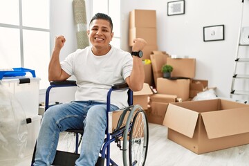 Young hispanic man sitting on wheelchair at new house screaming proud, celebrating victory and...