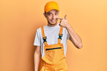 Hispanic young man wearing handyman uniform pointing with hand finger to face and nose, smiling cheerful. beauty concept