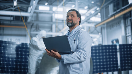 Male Engineer Uses Laptop Computer while Working on Satellite Construction. Aerospace Agency Manufacturing Facility: Scientists Develop, Assemble Spacecraft for Space Exploration, Observation Mission