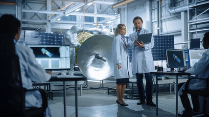 Engineer and Technician Talk, Use Laptop Computer while Working on Satellite Construction....