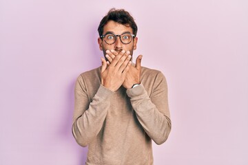 Handsome man with beard wearing turtleneck sweater and glasses shocked covering mouth with hands...