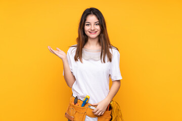 Young electrician woman over isolated on yellow background holding copyspace imaginary on the palm