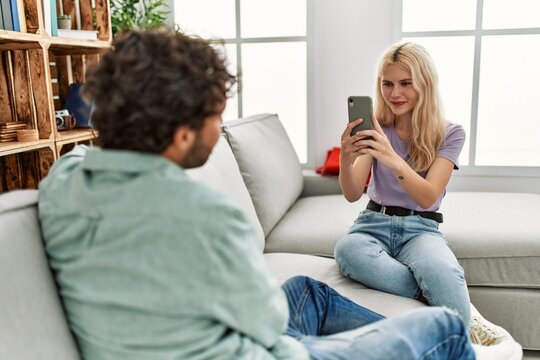 Young woman making picture of her boyfriend using smartphone at home