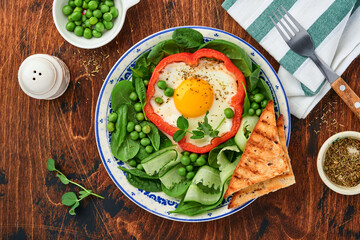 Red bell peppers stuffed with eggs, spinach leaves, green peas and microgreens on a breakfast plate on old wooden table background. Top view.