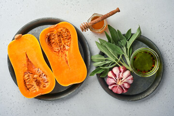 Halves of raw organic butternut squash with sage leaf, multicolored pepper garlic, honey, salt and pepper on a white slate, stone or concrete background. Food background. Top view with copy space.